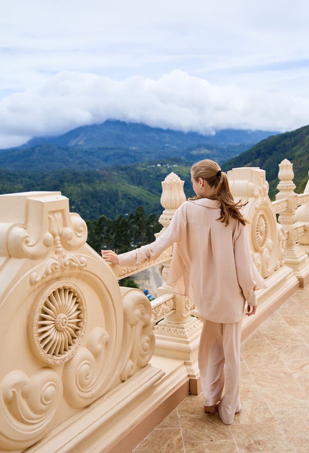 A visitor at the carved white balustrade of the Mahamevnawa Monastery terrace, looking out over the hills near Ella